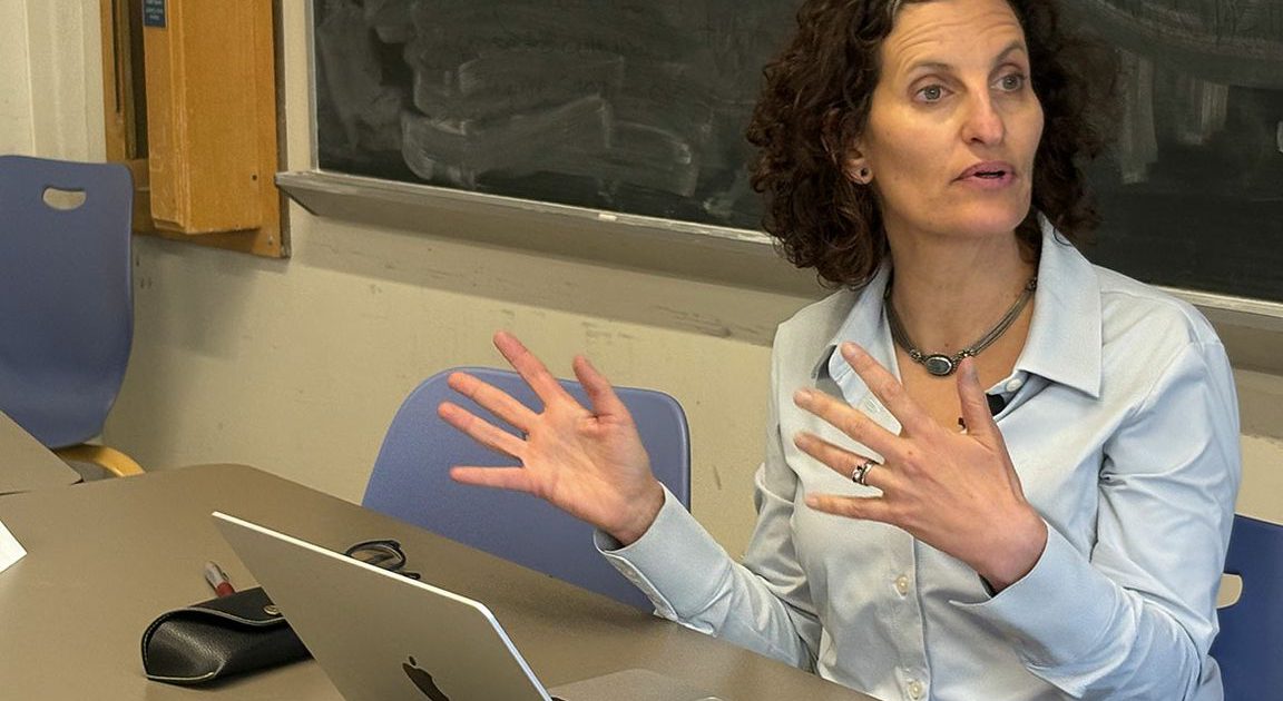 Professor Abigail Saguy sits at a table in front of a black board.